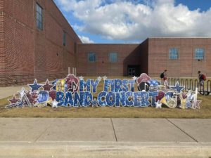 A festive display say "My First Band Concert" in front of a brick building