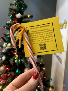 A candy cane attached to a card with a christmas tree behind